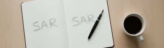 un bureau clair vu de dessus avec un carnet ouvert, un stylo plume posé en diagonale et une tasse de café, deux mots man