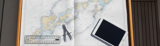 table à cartes d'un bateau de plaisance vue de dessus, carte marine papier dépliée, règle Cras et compas à pointes sèche